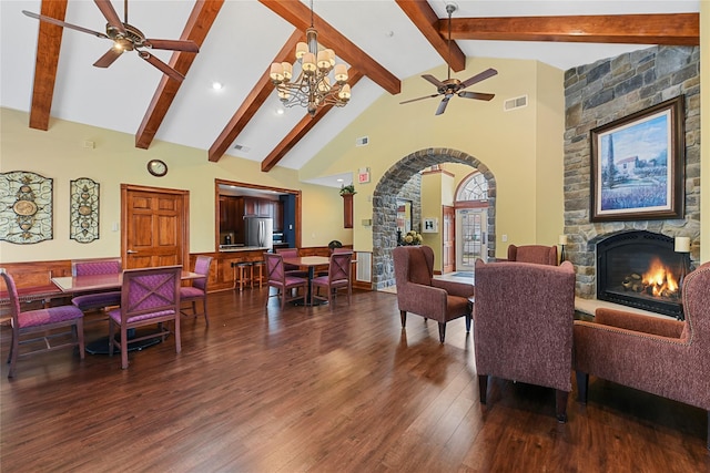 dining area featuring visible vents, a stone fireplace, ceiling fan with notable chandelier, wood finished floors, and high vaulted ceiling