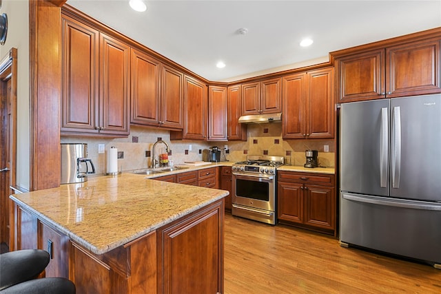 kitchen featuring light wood-style flooring, a sink, under cabinet range hood, stainless steel appliances, and a peninsula