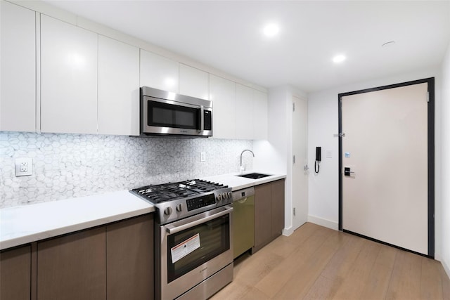 kitchen featuring light wood-style flooring, a sink, decorative backsplash, light countertops, and appliances with stainless steel finishes