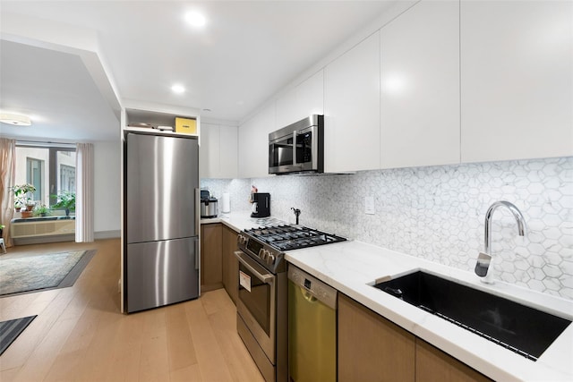 kitchen with light wood finished floors, backsplash, appliances with stainless steel finishes, modern cabinets, and a sink