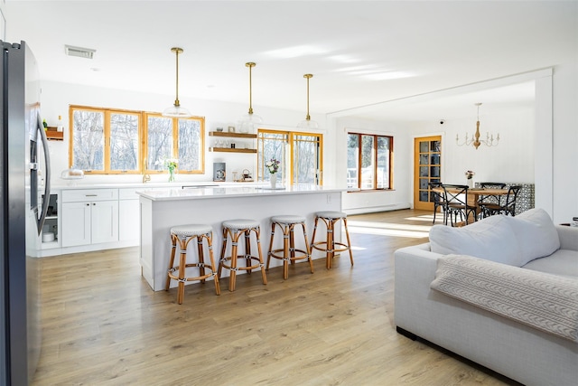 kitchen with visible vents, stainless steel refrigerator with ice dispenser, a kitchen breakfast bar, white cabinetry, and light wood-style floors