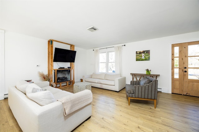 living area with a glass covered fireplace, visible vents, light wood-style flooring, and a baseboard radiator