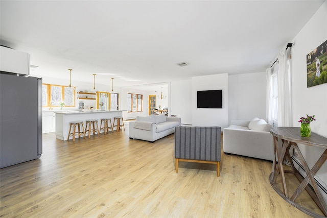 living area featuring light wood finished floors, visible vents, and a baseboard heating unit