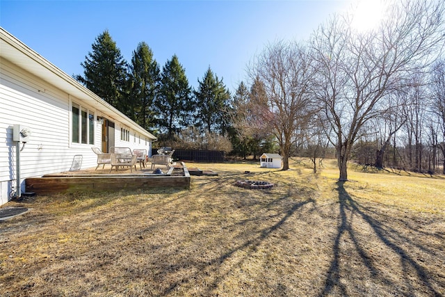 view of yard with fence, a shed, a wooden deck, an outdoor fire pit, and an outbuilding