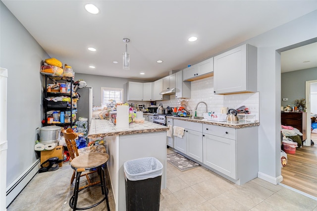 kitchen featuring backsplash, a baseboard heating unit, light stone countertops, under cabinet range hood, and a kitchen bar