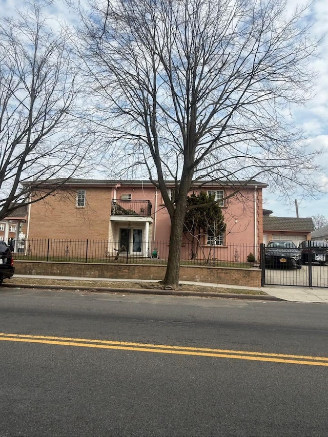 view of front facade featuring a balcony, brick siding, and a fenced front yard