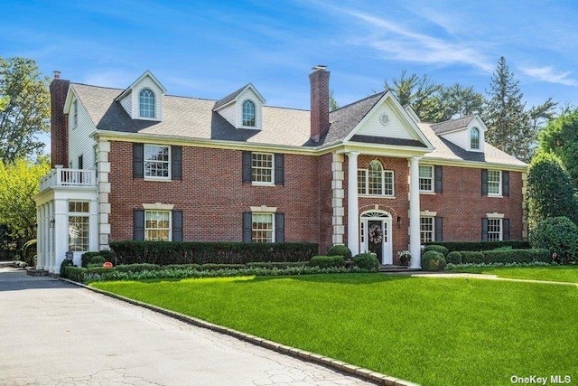 view of front of house featuring a front lawn, brick siding, and a chimney