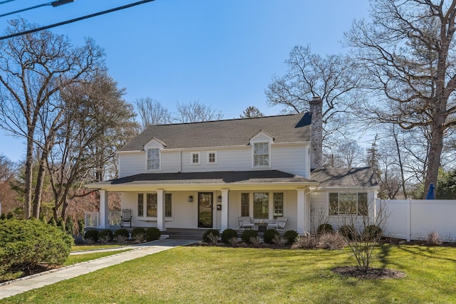 farmhouse with fence, a chimney, a front yard, roof with shingles, and a porch