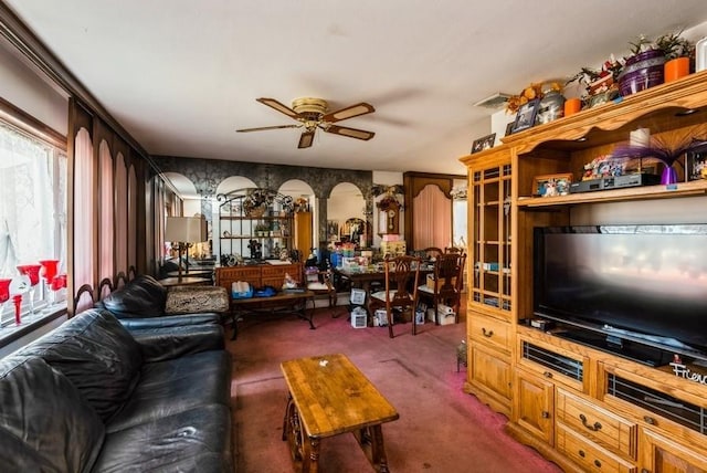 living area featuring arched walkways, carpet, and ceiling fan