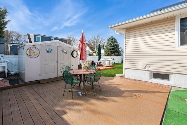 wooden deck with an outdoor structure, outdoor dining area, fence, and a storage unit