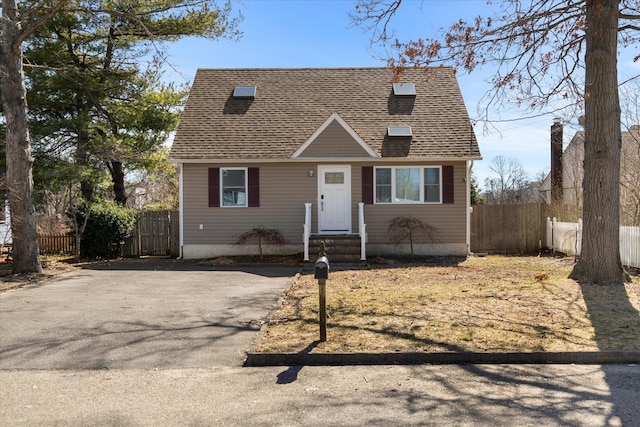 cape cod-style house with aphalt driveway, a shingled roof, and fence