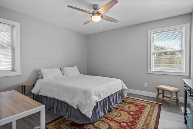 bedroom with multiple windows, a ceiling fan, baseboards, and wood finished floors