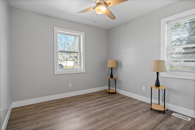 empty room featuring ceiling fan, visible vents, baseboards, and wood finished floors