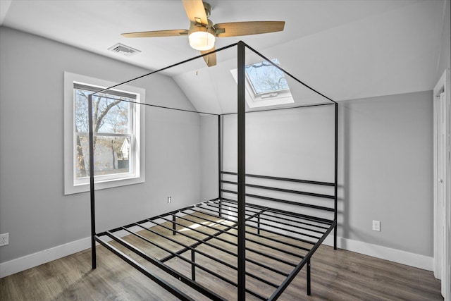 bedroom featuring visible vents, lofted ceiling with skylight, baseboards, and wood finished floors