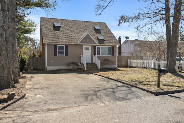 view of front of home with a shingled roof, driveway, and fence