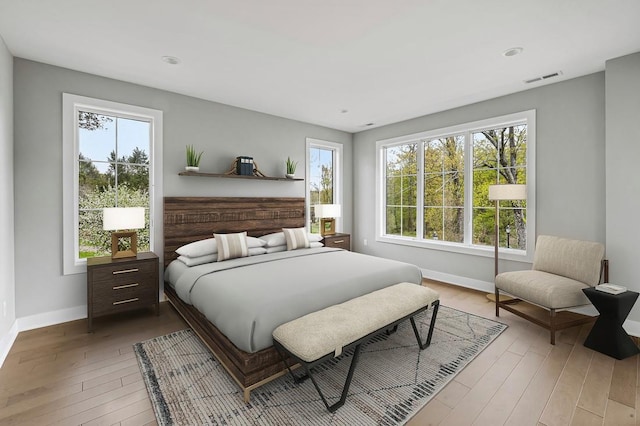 bedroom featuring visible vents, multiple windows, baseboards, and wood finished floors