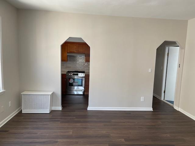 spare room featuring baseboards, arched walkways, and dark wood-type flooring