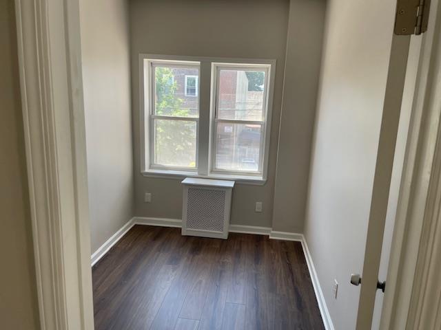 unfurnished room featuring radiator, dark wood-type flooring, and baseboards