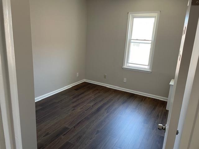 spare room with baseboards and dark wood-type flooring