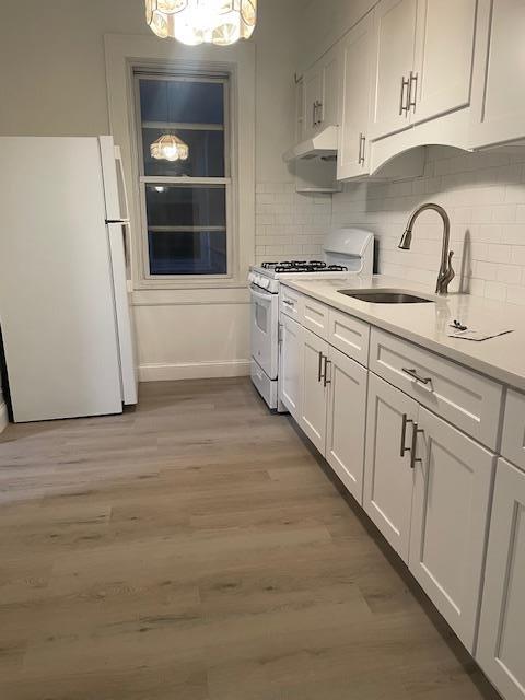 kitchen with under cabinet range hood, white appliances, light wood-style flooring, and white cabinetry