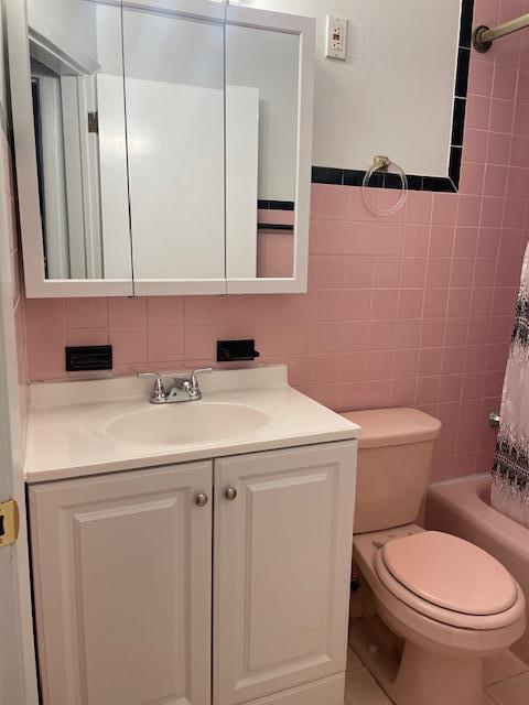 bathroom with toilet, tile walls, shower / bath combo, and vanity