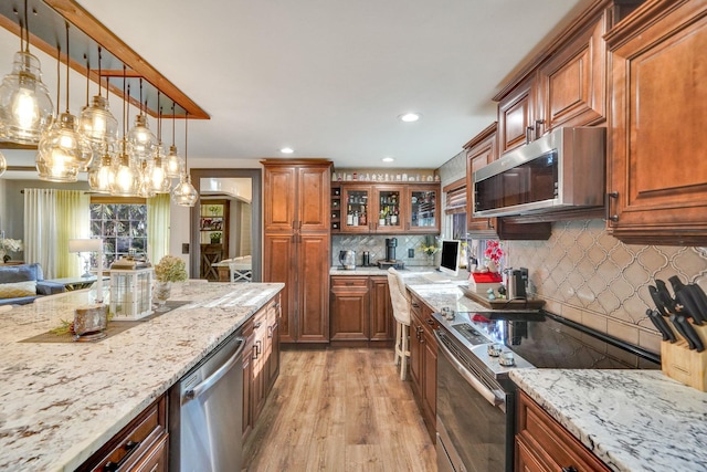 kitchen featuring light wood-type flooring, brown cabinets, pendant lighting, light stone counters, and stainless steel appliances