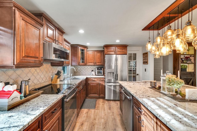 kitchen featuring light wood finished floors, light stone counters, appliances with stainless steel finishes, and a sink