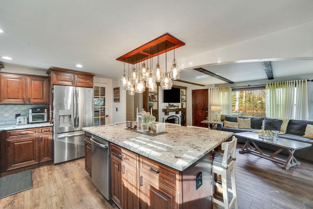 kitchen featuring light stone counters, stainless steel appliances, open floor plan, light wood-type flooring, and backsplash