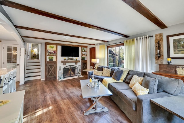 living area featuring stairs, beam ceiling, a fireplace with flush hearth, and wood finished floors