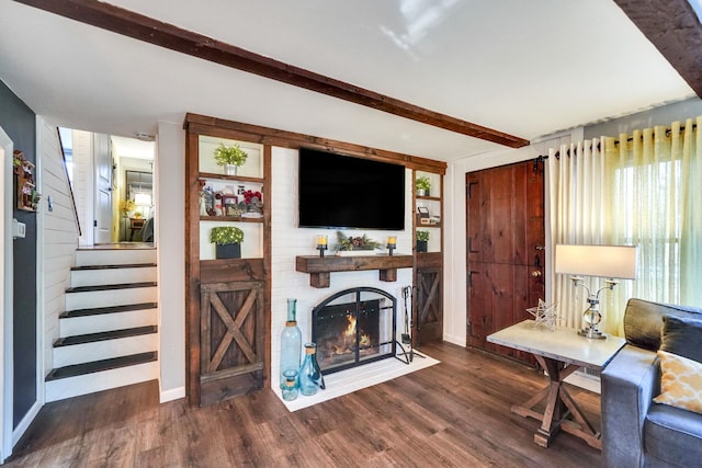 living room featuring beam ceiling, stairway, a fireplace, and wood finished floors