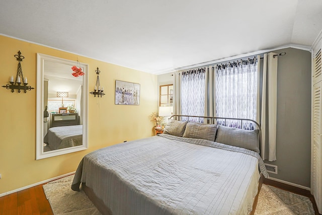 bedroom featuring visible vents, baseboards, lofted ceiling, and wood finished floors