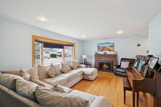 living area with recessed lighting, visible vents, a brick fireplace, and light wood finished floors