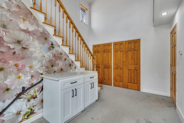 entrance foyer featuring light carpet, baseboards, stairs, and a towering ceiling