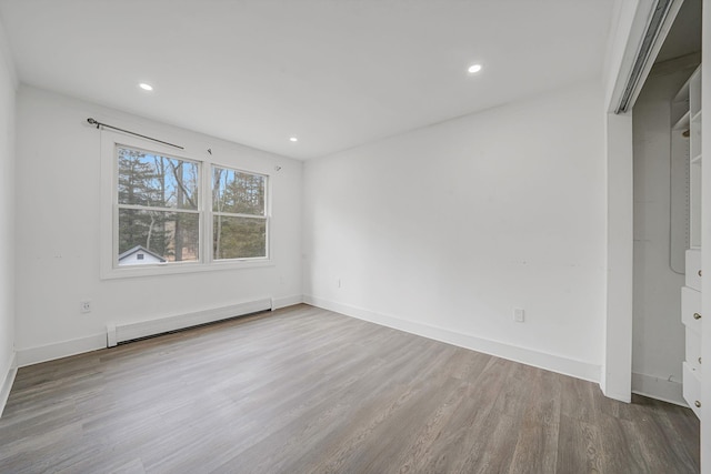 spare room with baseboard heating, recessed lighting, baseboards, and wood finished floors