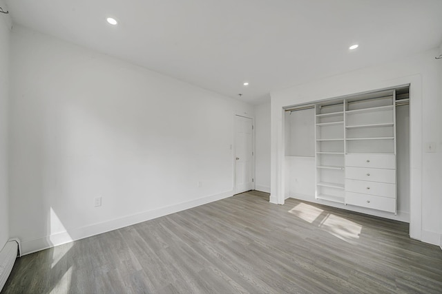 unfurnished bedroom featuring recessed lighting, a baseboard radiator, baseboards, and wood finished floors