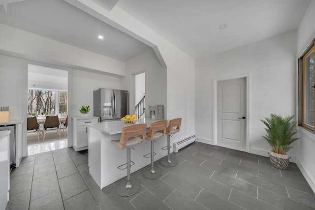 kitchen featuring stainless steel fridge with ice dispenser, a kitchen bar, light countertops, white cabinetry, and a baseboard radiator