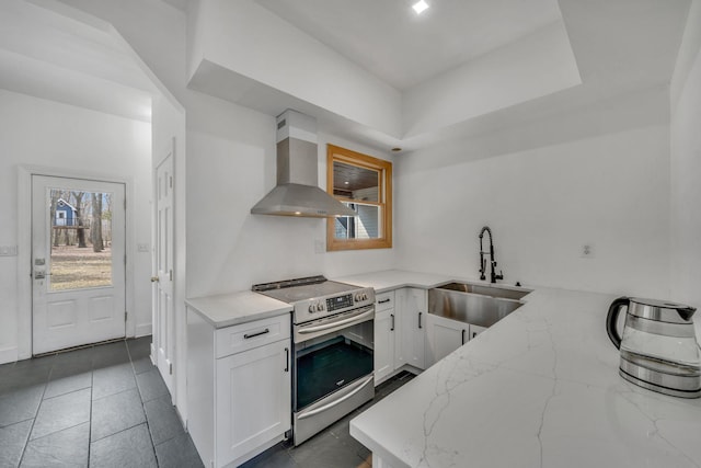 kitchen with stainless steel electric range oven, light stone counters, a sink, white cabinetry, and wall chimney range hood