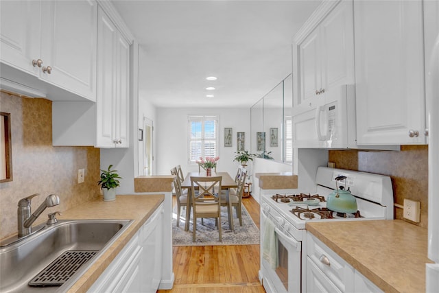 kitchen with white appliances, a sink, decorative backsplash, light countertops, and light wood-style floors