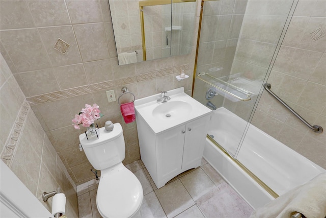 bathroom featuring toilet, vanity, tile patterned floors, combined bath / shower with glass door, and tile walls