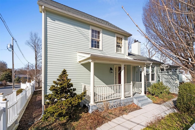 view of front facade featuring a porch, a chimney, and fence