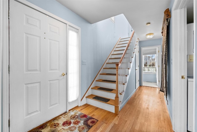 foyer entrance featuring stairs, light wood-type flooring, and baseboards