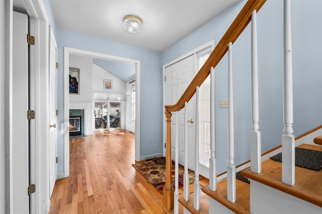 foyer entrance featuring a high end fireplace, light wood finished floors, baseboards, stairs, and vaulted ceiling