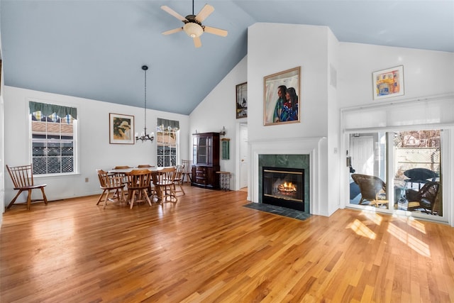 dining space with a high end fireplace, ceiling fan with notable chandelier, light wood finished floors, and a healthy amount of sunlight