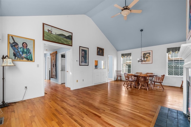 dining space with ceiling fan with notable chandelier, visible vents, light wood finished floors, and high vaulted ceiling