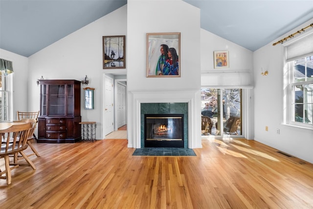 living area with visible vents, light wood-style flooring, a fireplace, and high vaulted ceiling