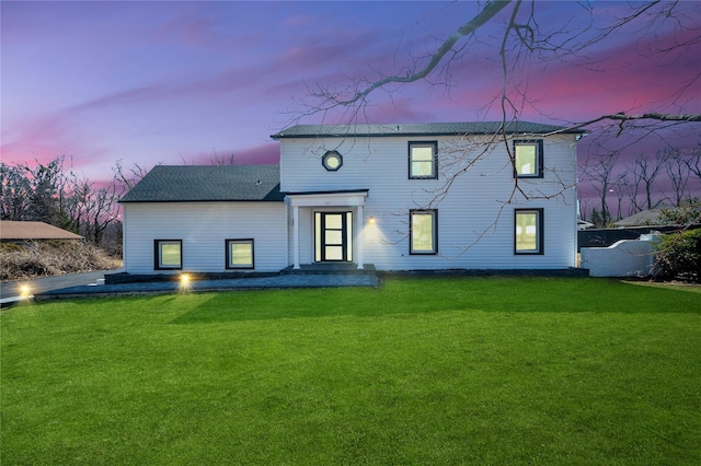 back of property at dusk with a yard