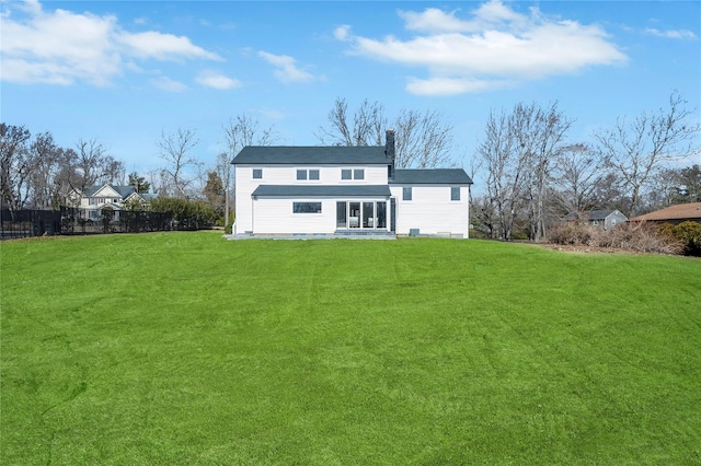 rear view of house with a chimney, a yard, and fence