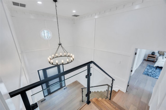 stairs featuring visible vents, an inviting chandelier, wood finished floors, and a decorative wall