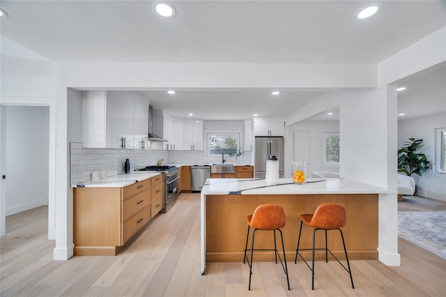 kitchen featuring a peninsula, a kitchen breakfast bar, appliances with stainless steel finishes, wall chimney range hood, and modern cabinets