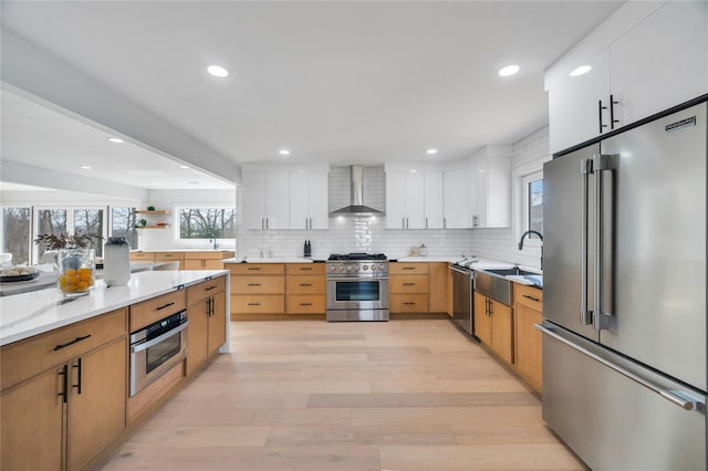 kitchen with high quality appliances, light wood-style flooring, a sink, wall chimney exhaust hood, and tasteful backsplash